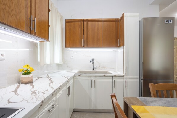 Una cocina con armarios de madera, un refrigerador de acero inoxidable, encimera de mármol y un lavamanos.