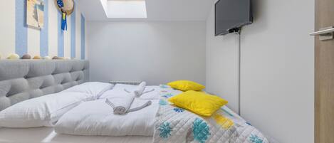 A bedroom with a bed, a flat-screen TV, a skylight, and a wall clock.