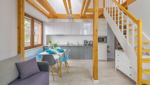 A modern kitchen with white cabinets, a dining area with blue chairs, and a wooden staircase. - Apartamenty Sun&Snow Villa Nautikka (Krynica Morska)