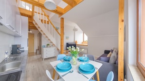 A modern kitchen with a built-in espresso machine, a dining area with blue plates and a vase of flowers, and a staircase leading to an upper level. - Apartamenty Sun&Snow Villa Nautikka (Krynica Morska)