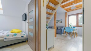 A modern bedroom with a bed, a TV, and a staircase leading to a dining area with a table and chairs. - Apartamenty Sun&Snow Villa Nautikka (Krynica Morska)