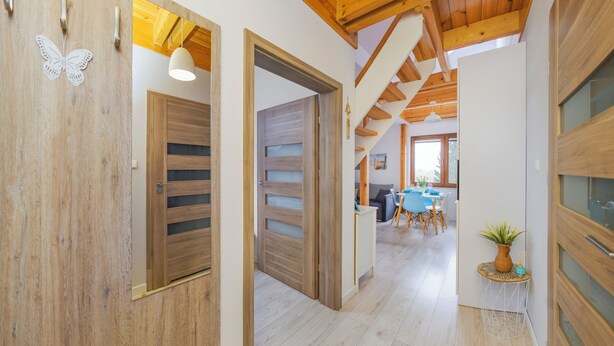 A hallway with wooden doors, a dining area with a table and chairs, and a plant on a side table. - Apartamenty Sun&Snow Villa Nautikka (Krynica Morska)