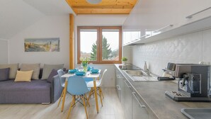 A modern kitchen with a built-in oven, a dining area with a table and chairs, and a sofa with cushions. - Apartamenty Sun&Snow Villa Nautikka (Krynica Morska)