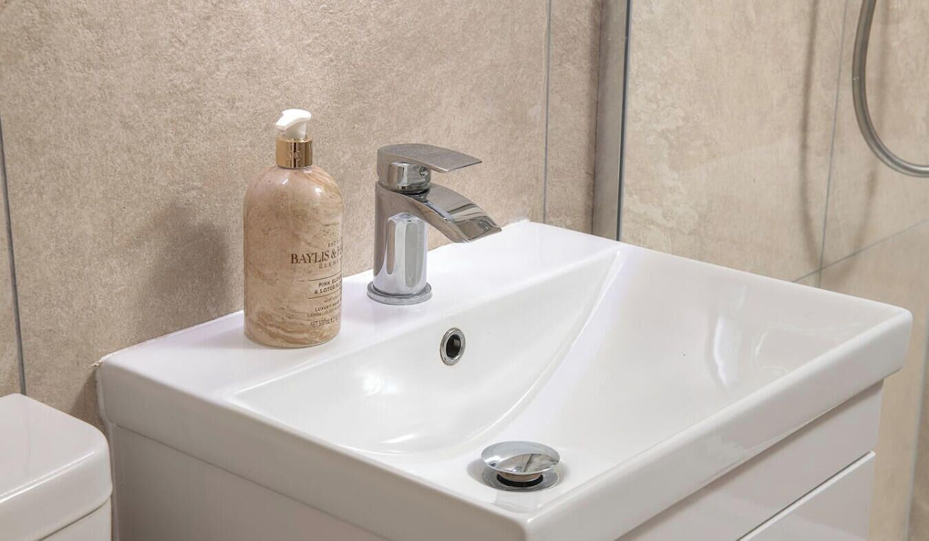 Ein Badezimmer mit einem weißen Waschbecken, einem silbernen Wasserhahn und einer Lotion von Baylis & Perkins.