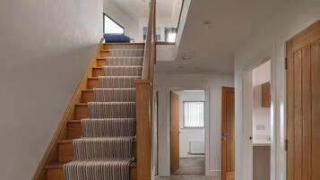 A staircase with wooden steps and carpeted handrails, leading to a room with a window and a door.