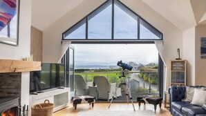 A living room with a fireplace, a television, a large window, and a telescope.