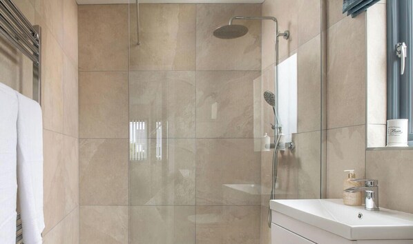 A modern bathroom with a glass-enclosed shower, a white vanity with a mirror, and a bottle of soap on the counter.