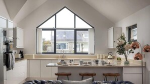 A modern kitchen with a large window, white cabinetry, and a central island with stools.