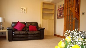 A living room with a leather sofa, a wooden cabinet, a lamp, and a painting on the wall.