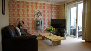 A living room with a sofa, a coffee table with flowers, a flat-screen TV, and a fireplace.