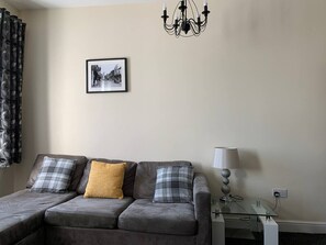 Un salon avec un canapé, une lampe, un tableau au mur et un lustre.