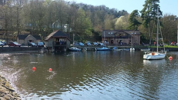 Une jetée au bord du lac avec des bateaux, un petit bâtiment et une plus grande construction dotée d’un balcon.