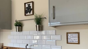Une cuisine dotée d’un évier en acier inoxydable, d’un dosseret de carrelage blanc, d’un plan de travail en bois, de deux plantes en pot, d’un réfrigérateur en acier inoxydable et d’une affiche encadrée accrochée au mur.