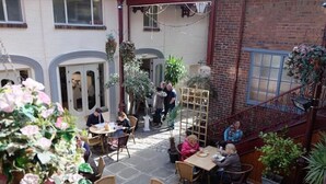 Un café en plein air avec des tables et des chaises, entouré de plantes en pot et d’un mur de briques.
