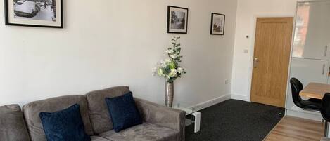 A living room with a sofa, a dining table, and a vase of flowers.