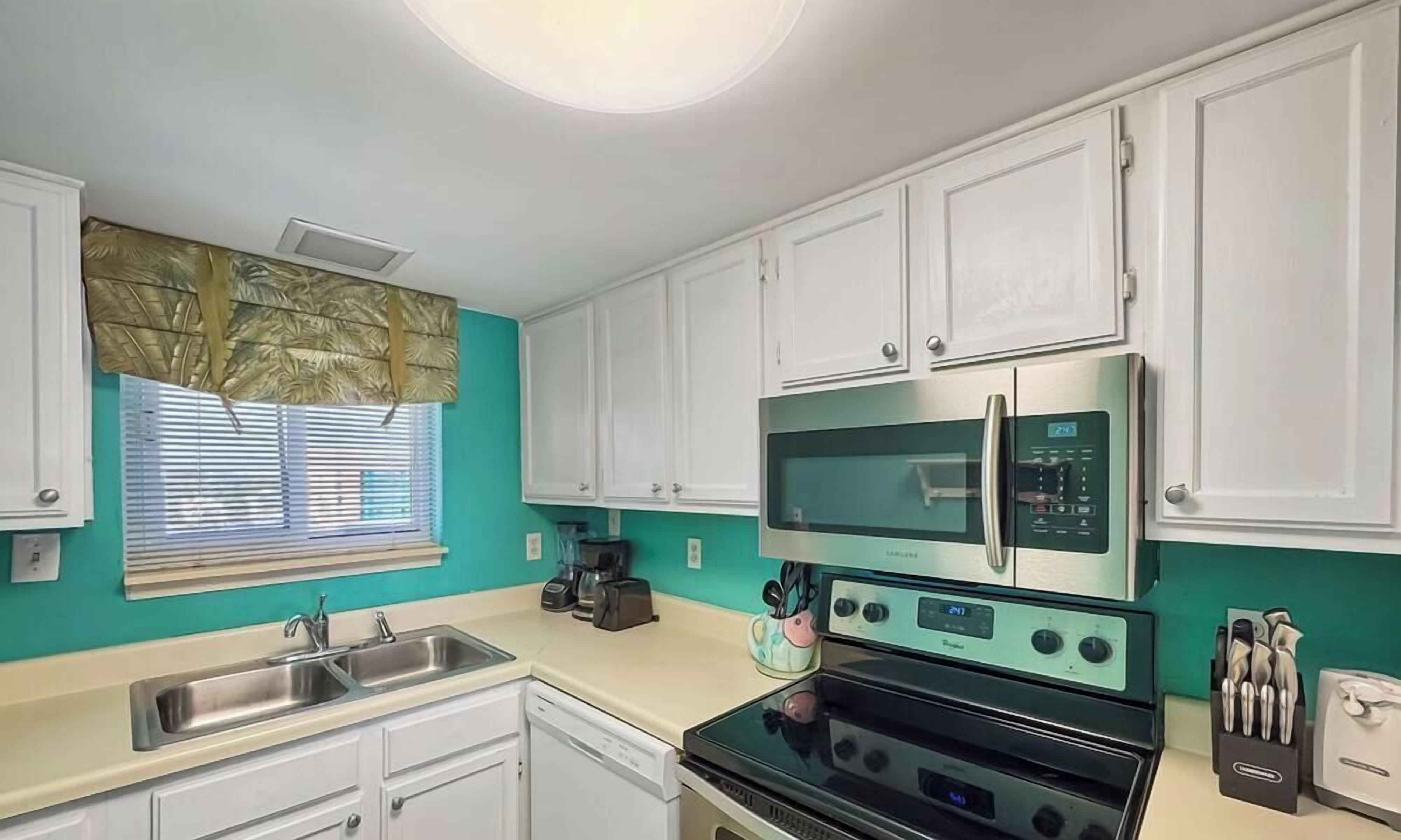 A kitchen with white cabinets, a stainless steel microwave, a black stove, and a window with blinds.