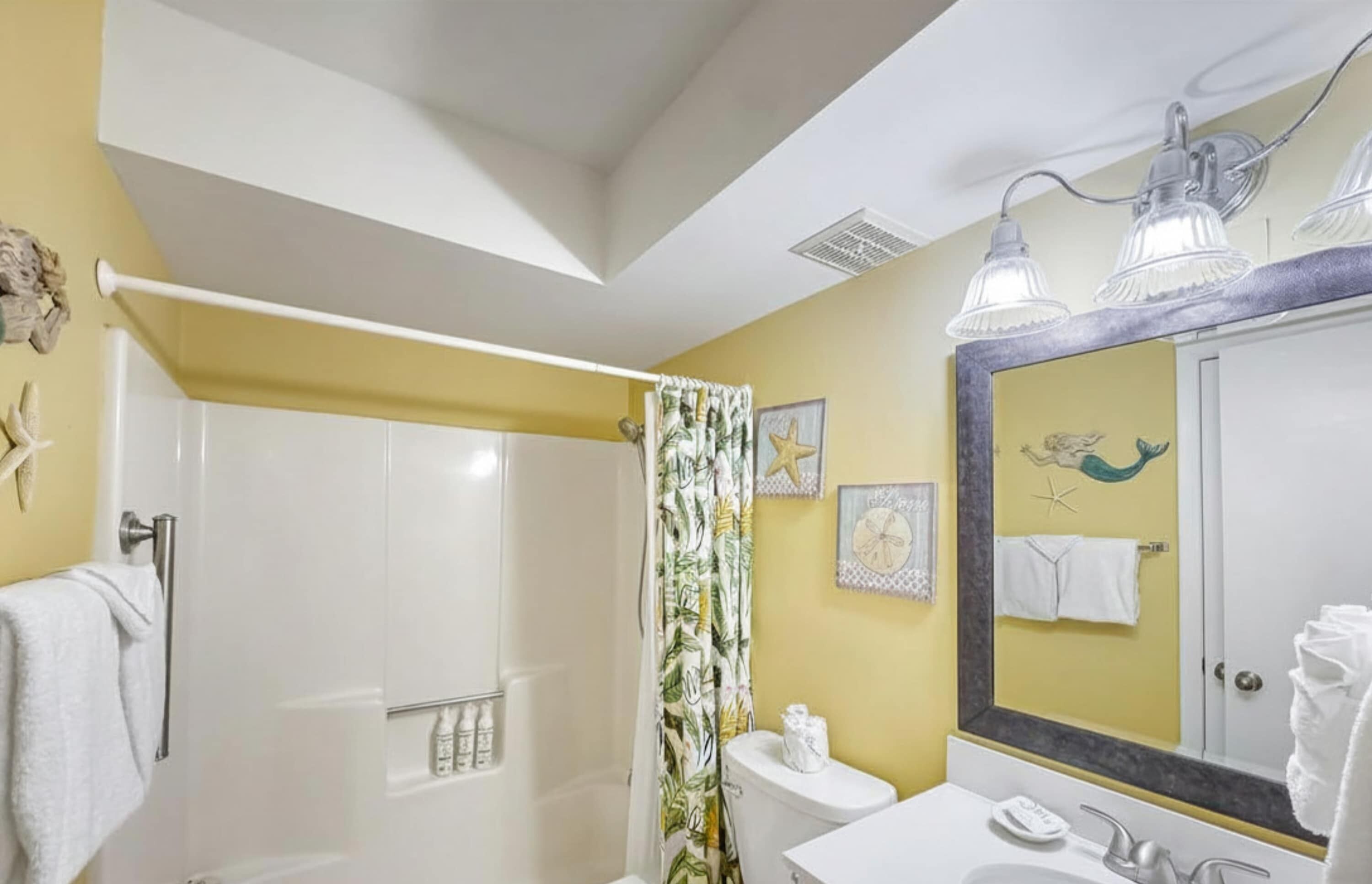 A bathroom with a shower, toilet, sink, and a large mirror.