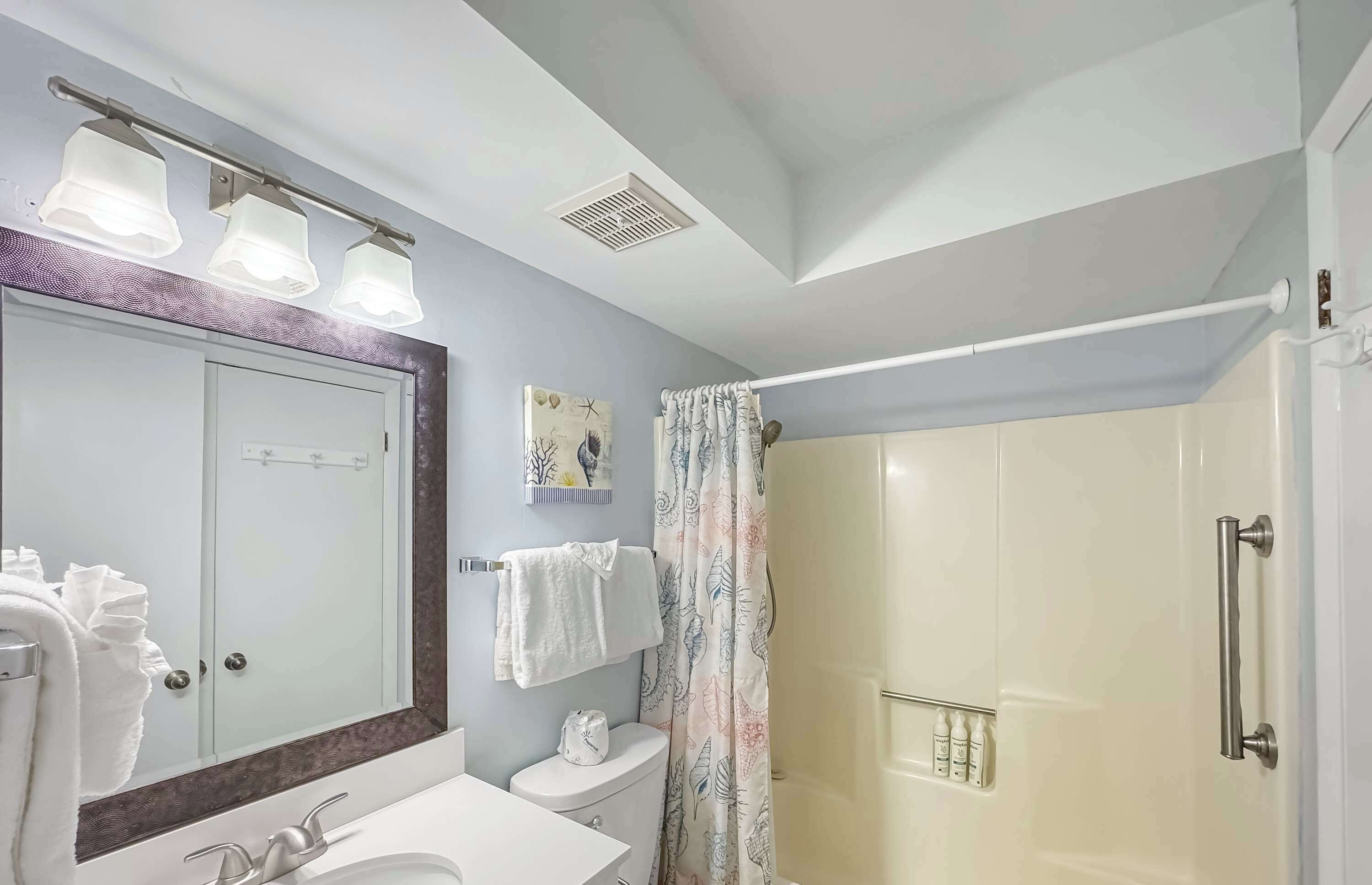 A bathroom with a large mirror, a sink, a toilet, a shower with a curtain, and a towel rack.