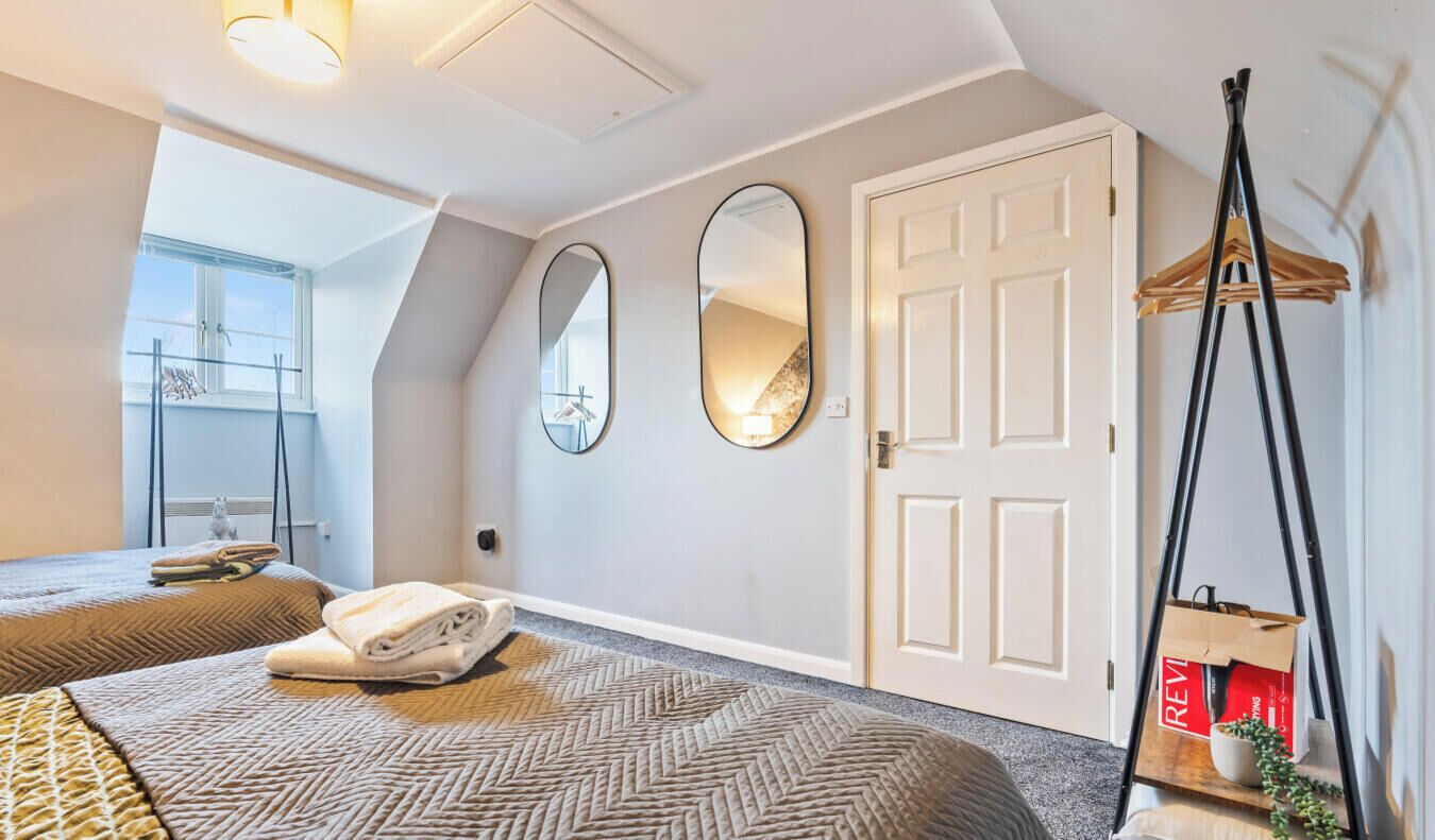 A hotel room with two beds, a large mirror, a door, and a hanging chair.