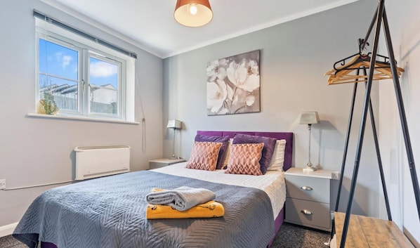 Quarto com cama, mesas de cabeceira, radiador, janela e luminária pendente.