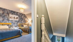 Quarto com duas camas, parede com padrão floral e escada com balaústres brancos.