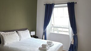 Un dormitorio con cama, ventana con cortinas, luz de techo y radiador.