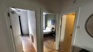 Un pasillo que conduce a un dormitorio con cama, mesita de noche y lámpara de pared.