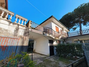 Ein zweistöckiges Gebäude mit Balkon, Tor und kleinem Garten.