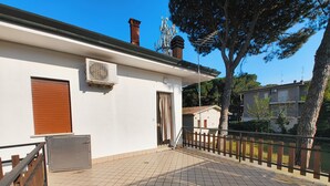 Eine geflieste Terrasse mit Metallgeländer, einer Holztür und einem Schornstein.