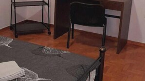 Una habitación con una cama, un escritorio de madera, una silla y un estante en la pared.