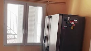 Una habitación con un ventanal grande, aire acondicionado de pared y un refrigerador.