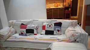 Un sofá con tapicería floral, una manta a rayas y cojines estampados en una habitación con una cocina al fondo.