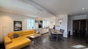 A modern living room with a yellow sofa, a dining table with chairs, a kitchen area, and a hallway leading to another room. - Vacation apartment Marienplatz (Garmisch-Partenkirchen)