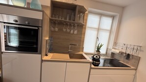 A modern kitchen with built-in appliances, a sink, and a window with blinds. - Vacation apartment Marienplatz (Garmisch-Partenkirchen)