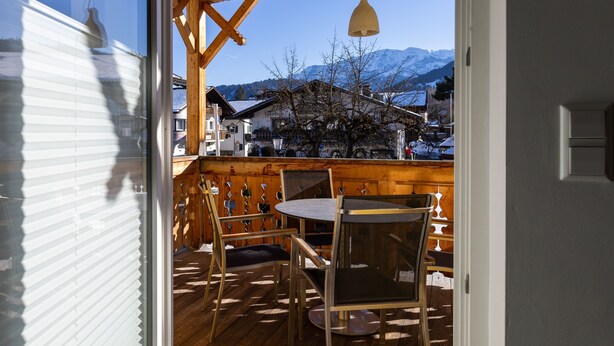 A wooden deck with a table and chairs, a hanging light fixture, and a view of snow-capped mountains in the background. - Vacation apartment Marienplatz (Garmisch-Partenkirchen)