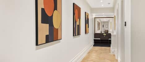 Un pasillo con obras de arte en las paredes, piso de madera y vista a una habitación con escritorio y silla.