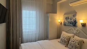 A hotel room with a bed, curtains, a painting, and a ceiling light. - HERA BUTİK OTEL (Bozcaada)