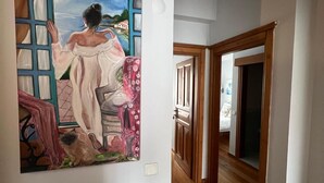 A hallway with wooden flooring, a painting on the wall, and a door leading to another room. - HERA BUTİK OTEL (Bozcaada)