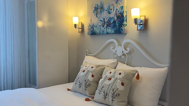A bedroom with a bed, pillows, a painting, and wall-mounted lights. - HERA BUTİK OTEL (Bozcaada)