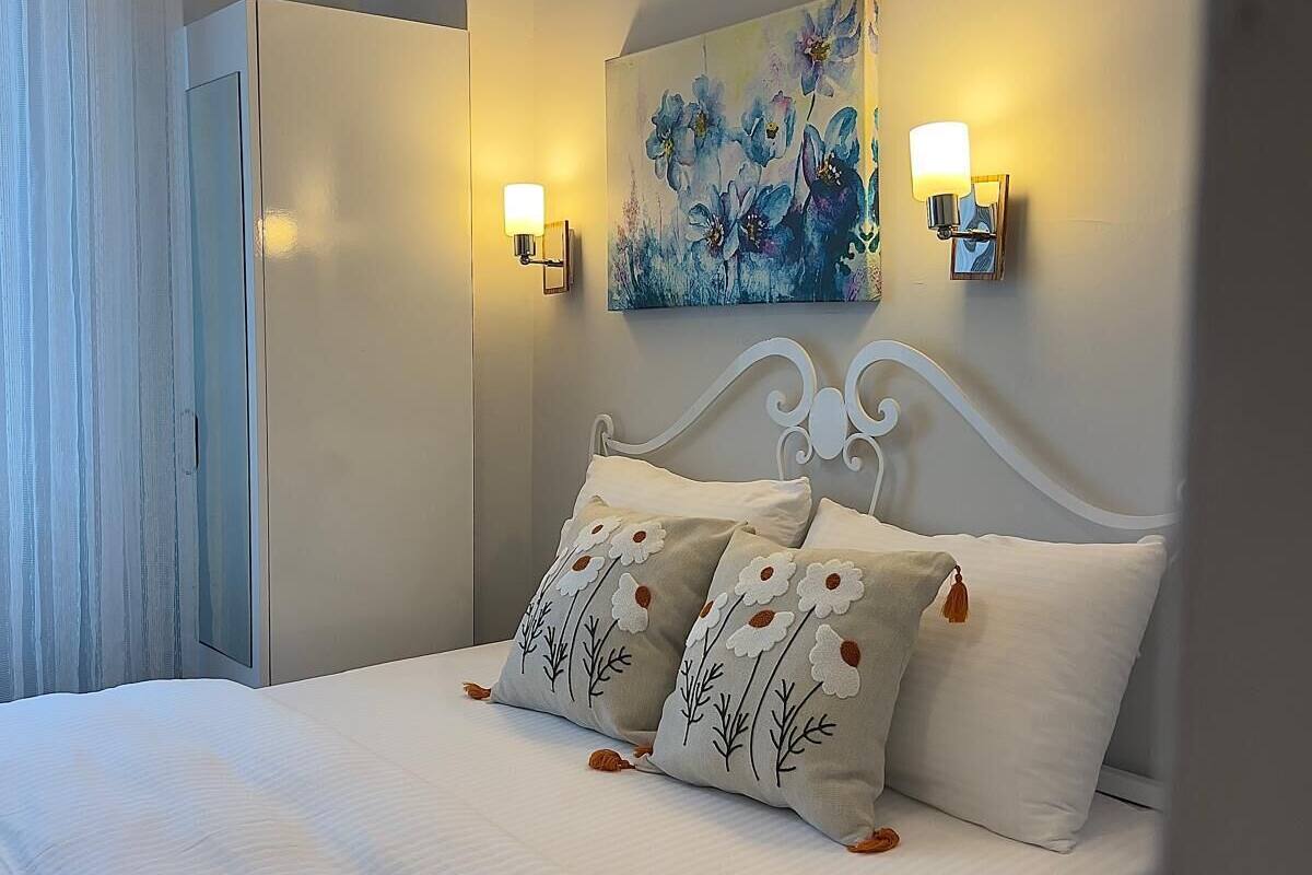 A bedroom with a bed, pillows, a painting, and wall-mounted lights.