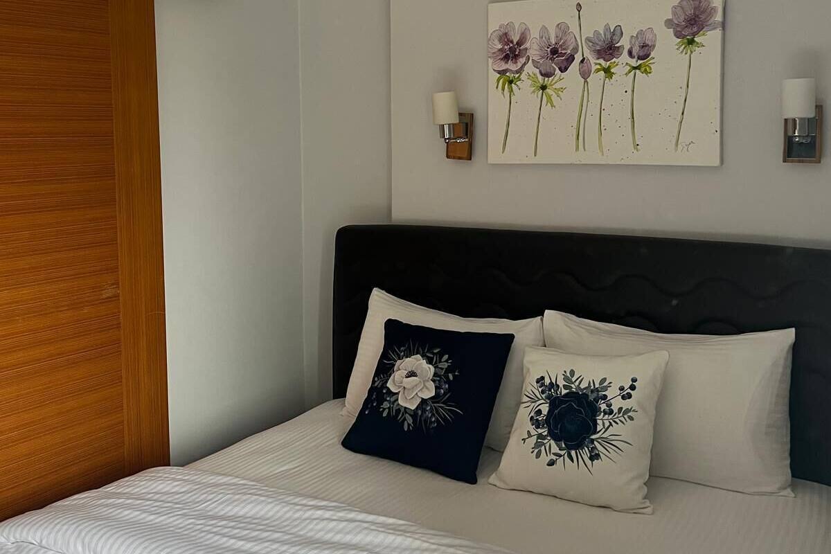 A bedroom with a bed, an air conditioner, a wall-mounted artwork of flowers, and a nightstand with a candle.