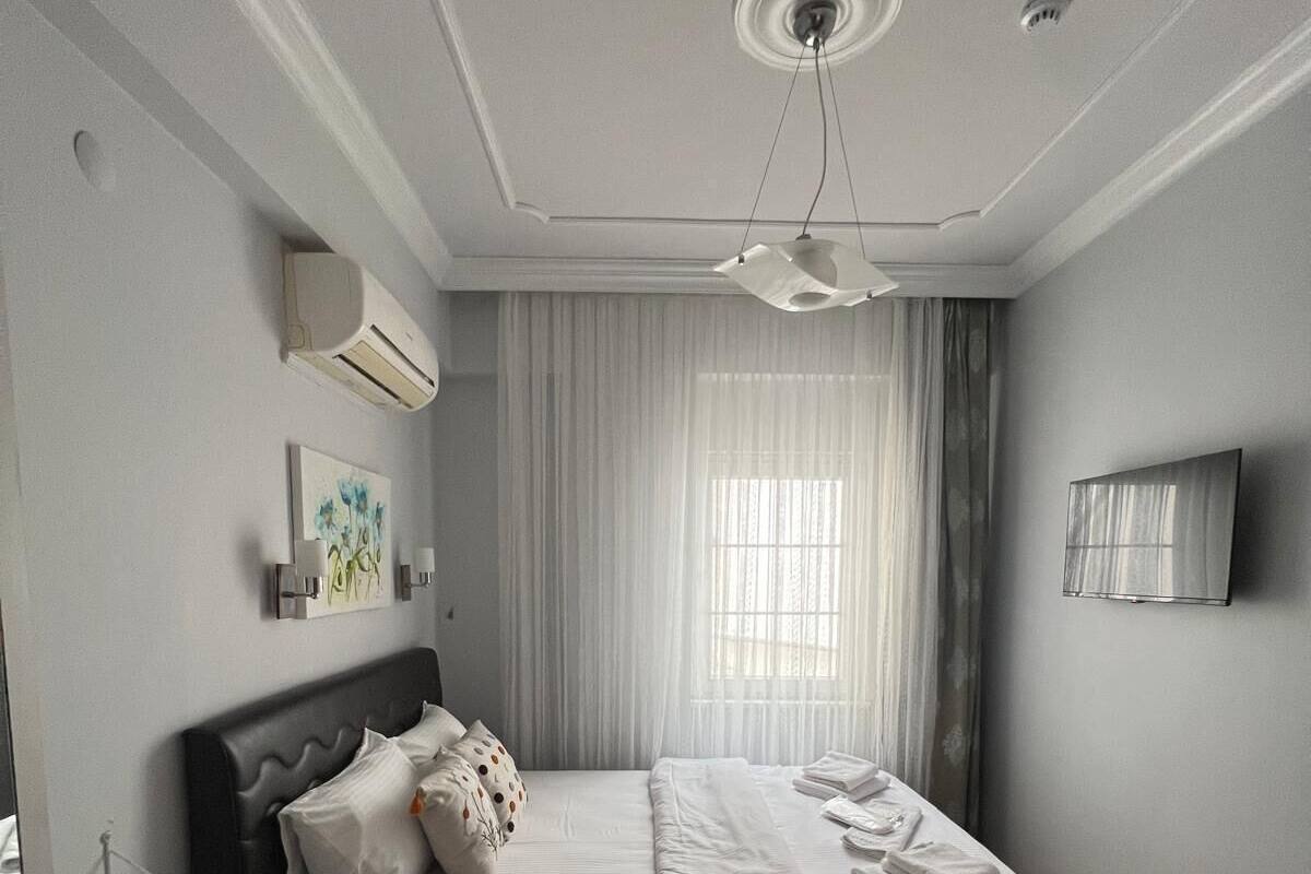 A modern hotel room with a bed, bedside table, air conditioning unit, and a television on the wall.