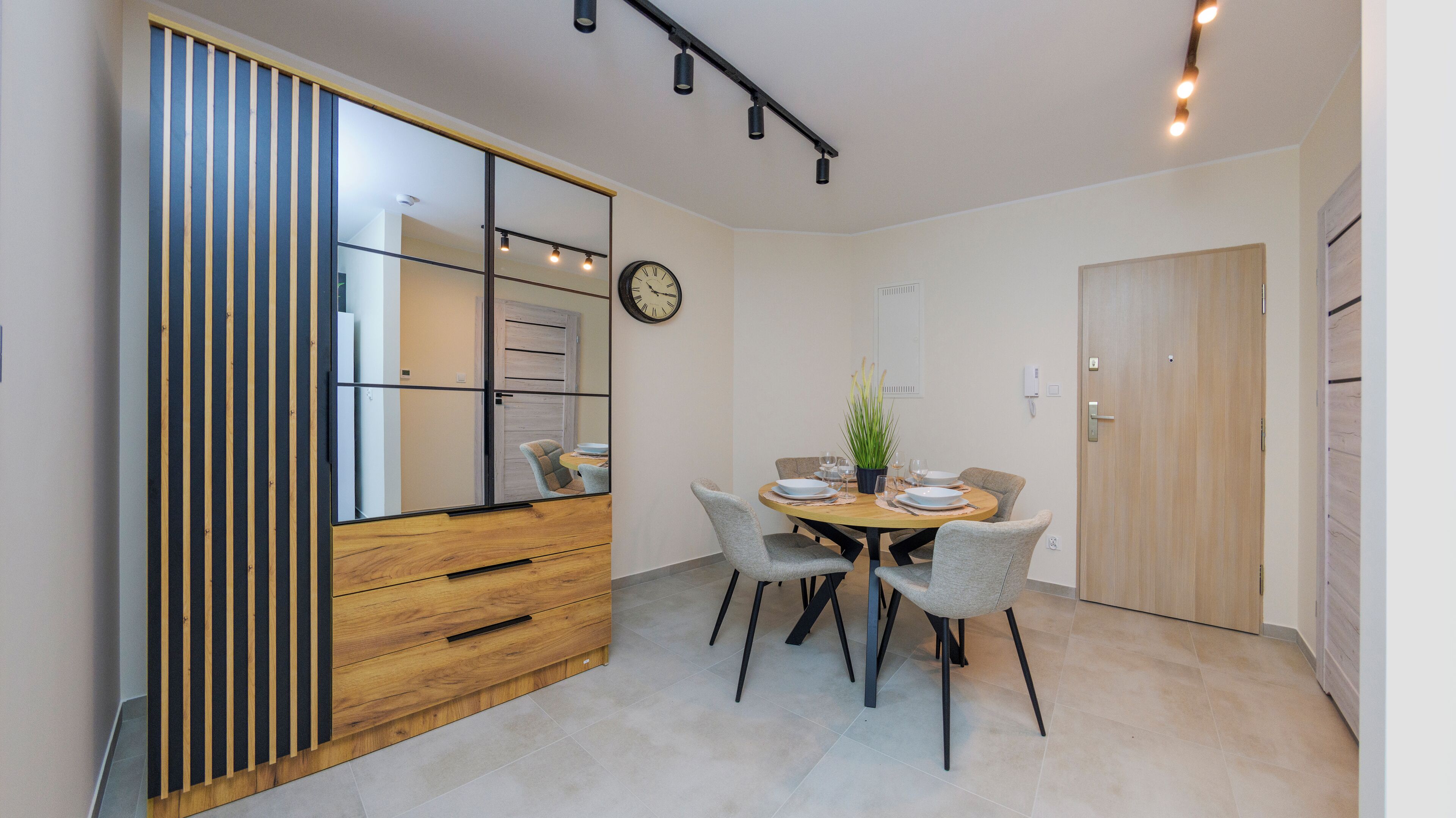 Un coin repas avec une table en bois, quatre chaises, une horloge et un miroir.
