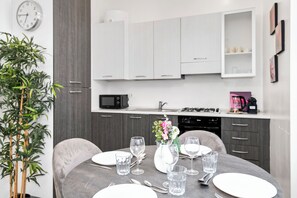 Une cuisine moderne avec des meubles blancs, un four à micro-ondes et une table à manger dressée avec des assiettes, des verres et des couverts.