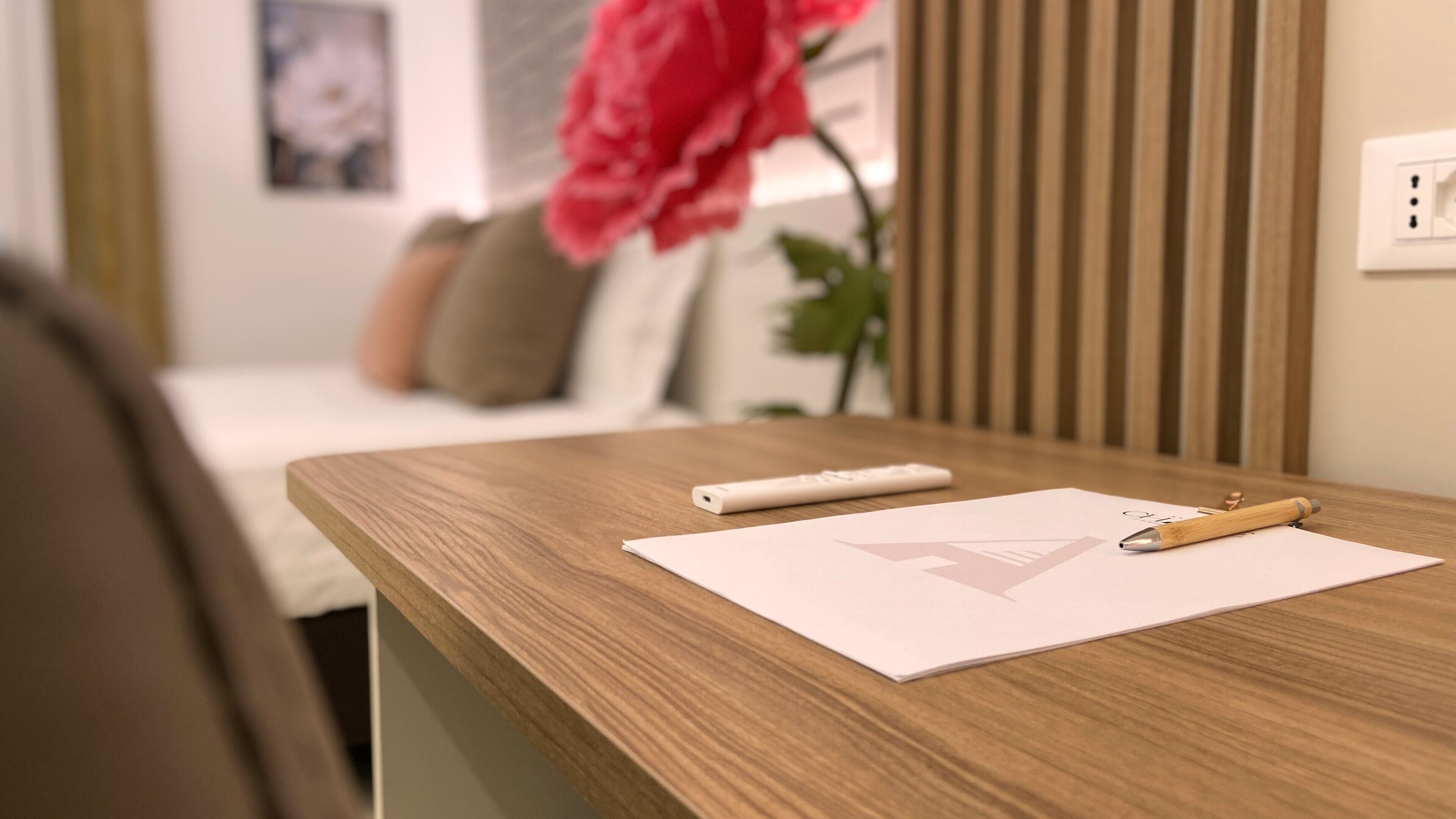 A wooden desk with a remote control, a pen, and a piece of paper with a logo.
