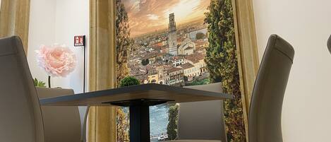 A dining area with a table and chairs, a large painting of a cityscape, and a fire exit sign.