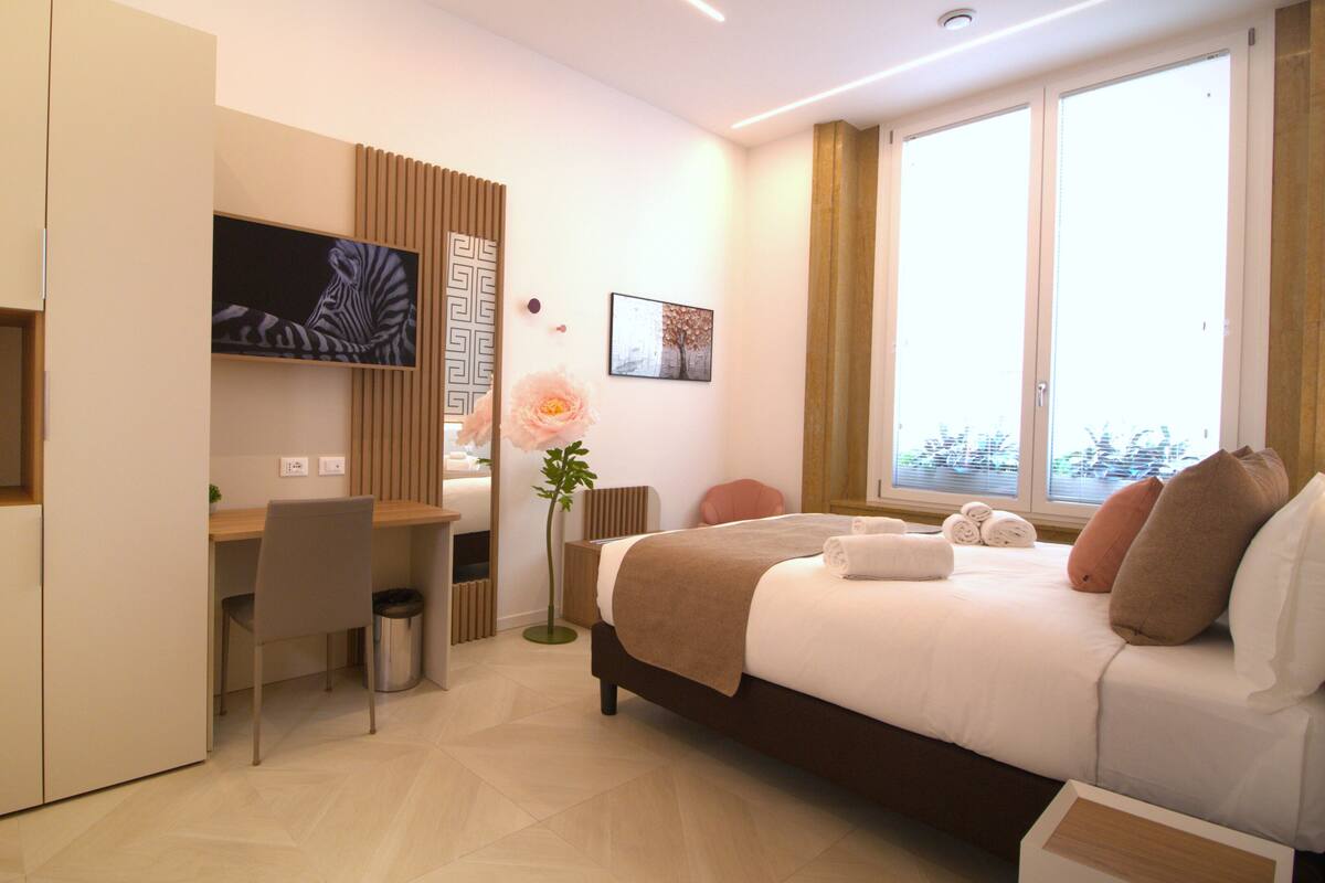 A hotel room with a bed, a desk, a chair, a TV, and a window.