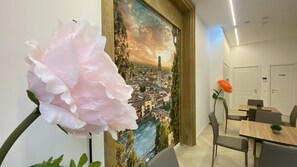 A room with a large floral arrangement, a cityscape mural, a dining area with chairs and a table, and a door with a nameplate. - Charme Flower Rooms (Verona)