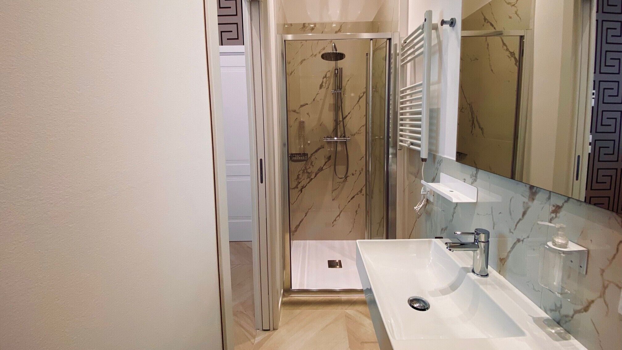 A bathroom with a glass-enclosed shower, a white sink, and a marble backsplash.