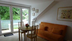 Een kamer met een eettafel, stoelen, een oranje bank, een lamp en uitzicht door een schuifdeur.